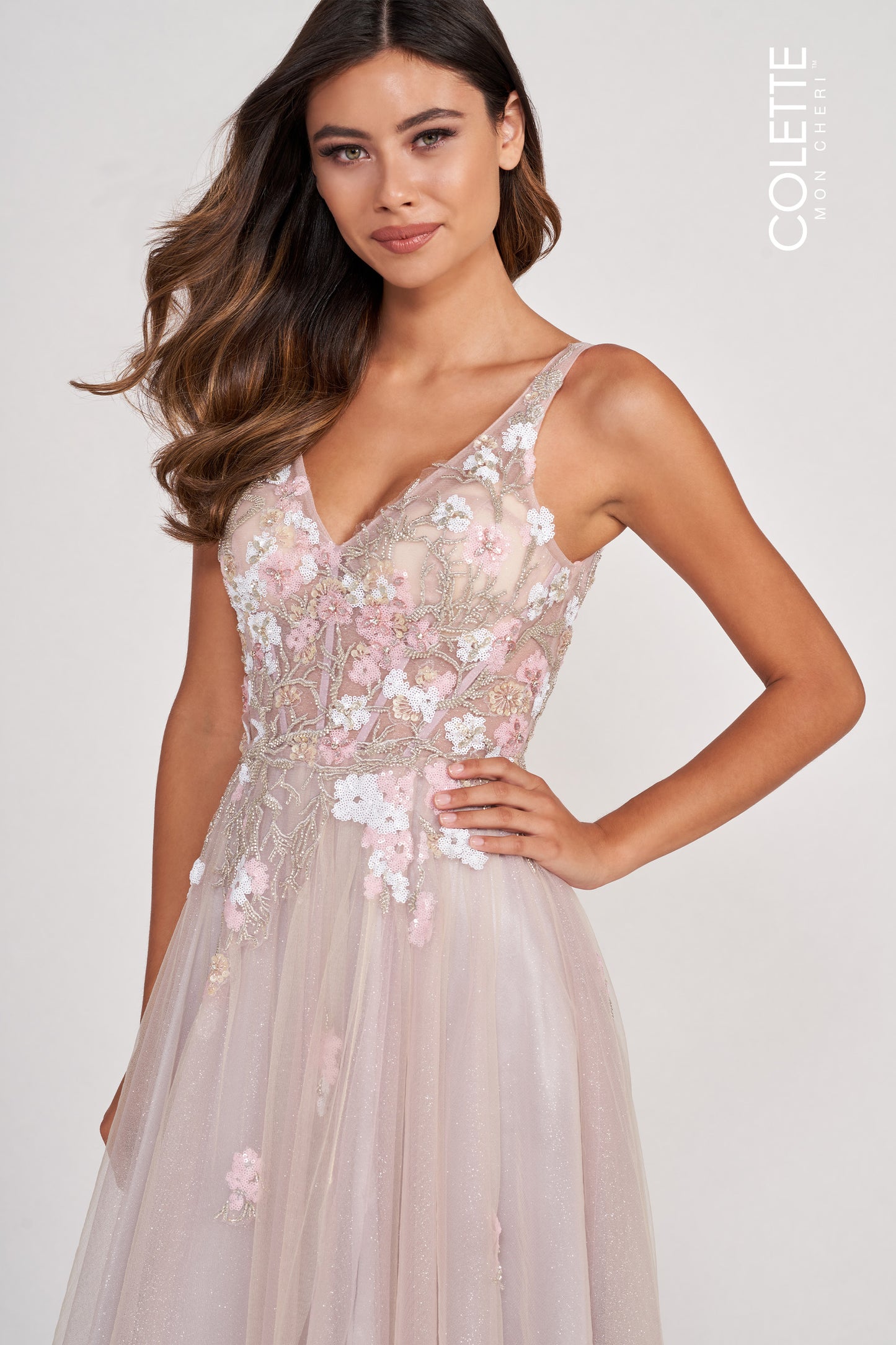 Brunette Model standing in silver multi colored prom dress with one hand on hip. Dress features Tulle Fabric, Sheer Corset Bodice, Flowy Skirt, Slit, Lace-Up Back